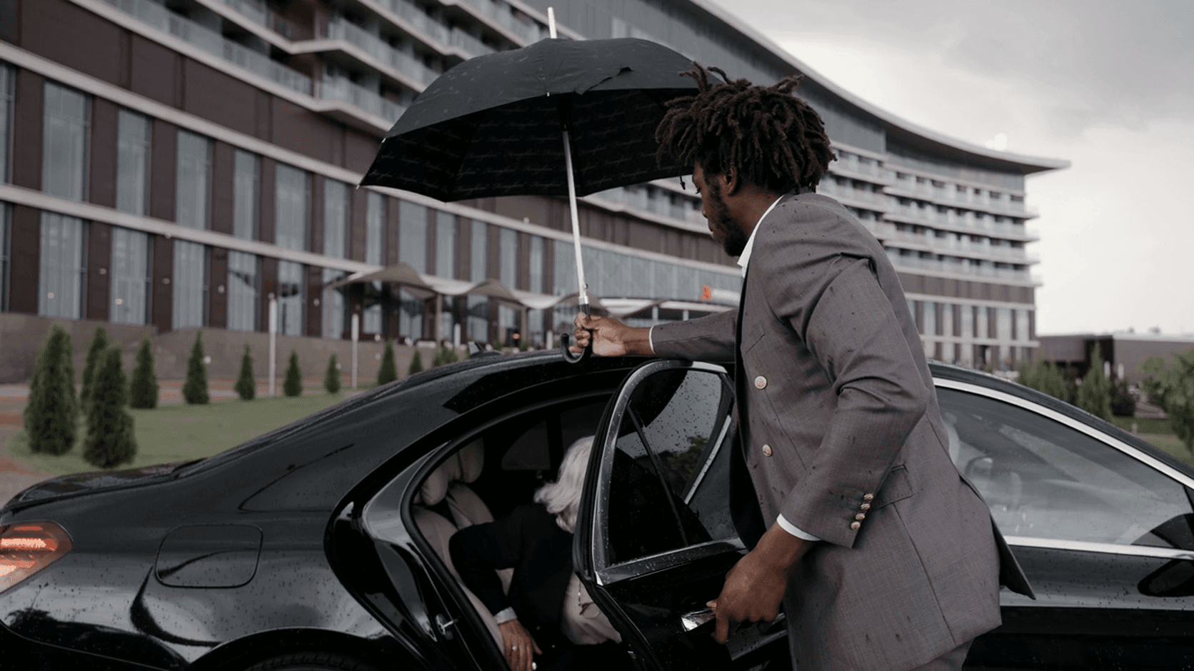 Chauffeur holding an umbrella while opening the rear door of a sedan for a passenger
