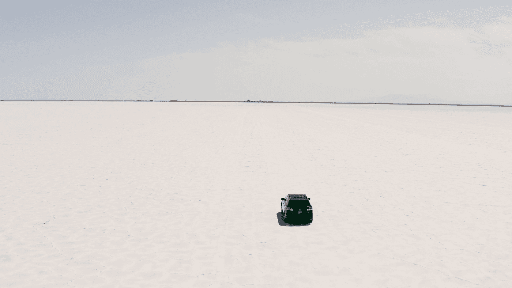 Aerial view of a single black car driving across a white salt flat