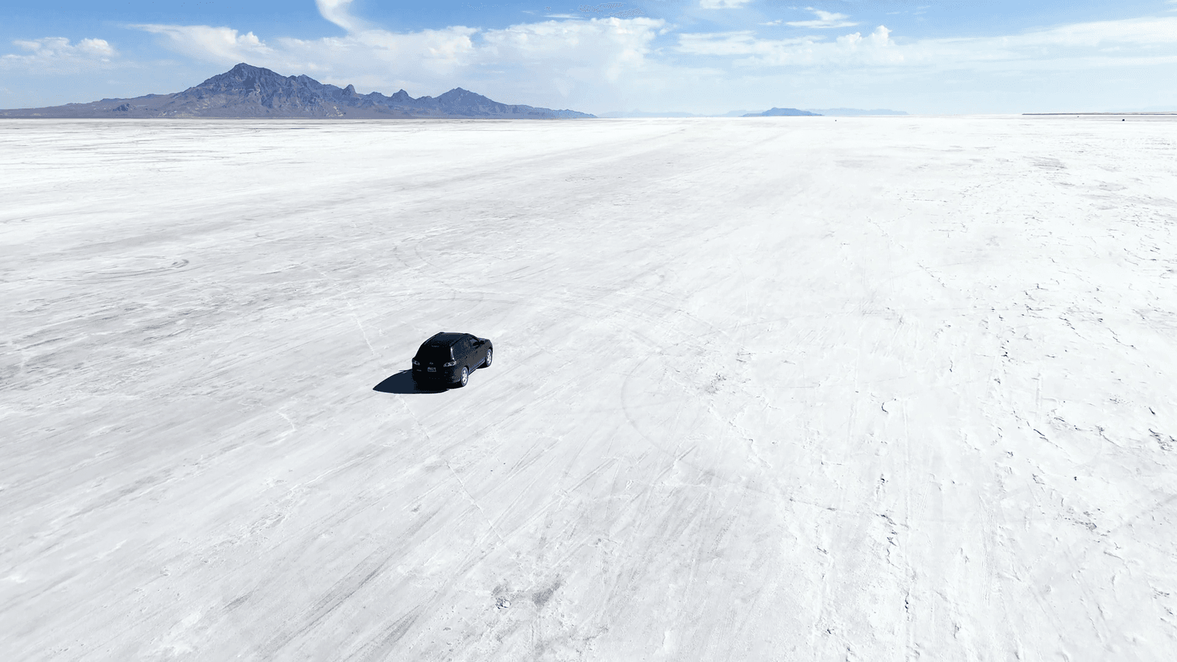 Aerial view of a black car alone on a vast white salt flat