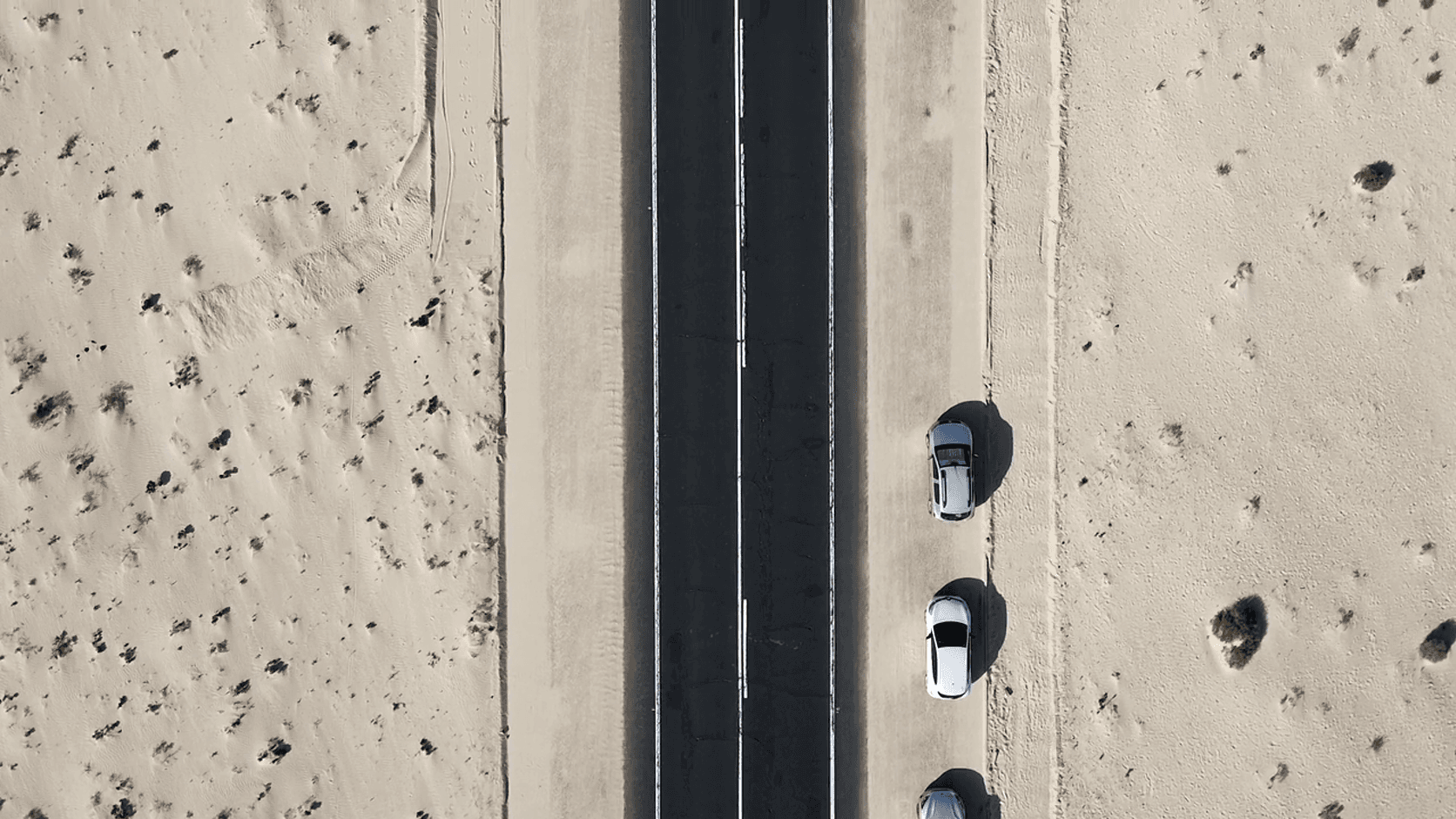 Top-down aerial view of vehicles parked beside a straight desert road
