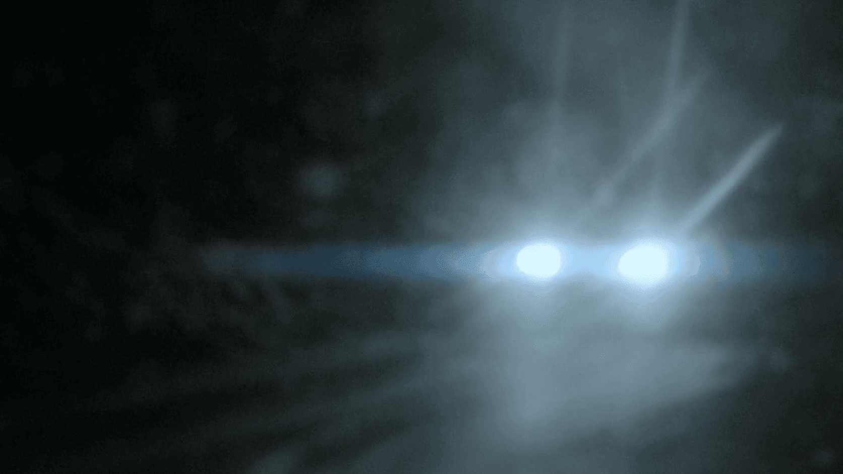 Headlights glowing through falling snow on a dark road